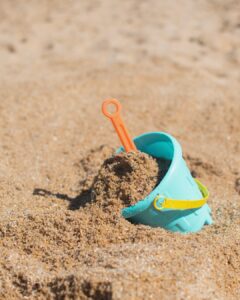 A plastic bucket filled with sand on a beach. Photo by Heather McKean on Unsplash.